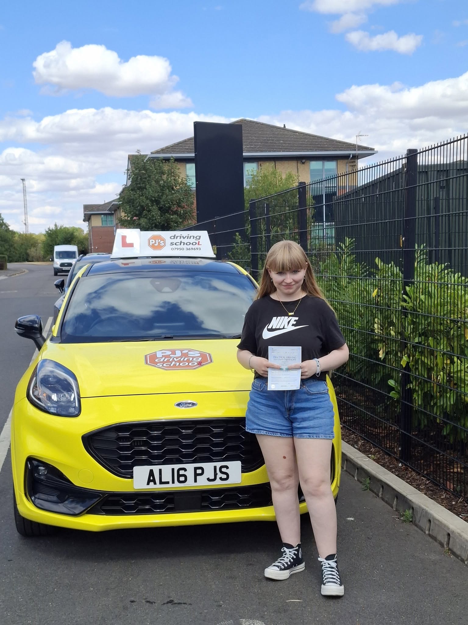 Learner celebrating a driving test pass beside PJ's yellow lesson car